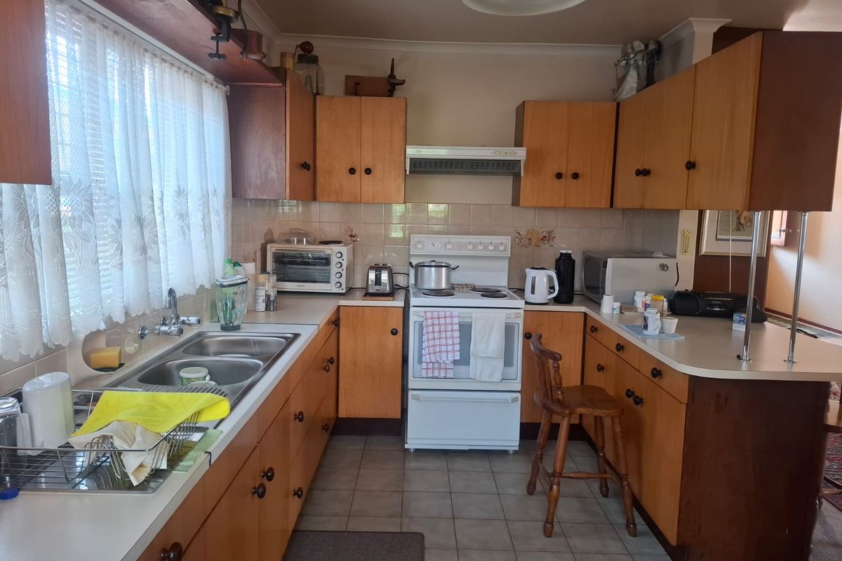 A dated kitchen featuring original timber-look laminate cabinetry, a freestanding electric stove, and a double bowl sink with tiled splashbacks.