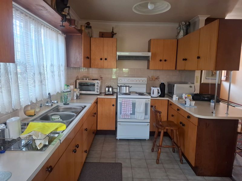 A dated kitchen featuring original timber-look laminate cabinetry, a freestanding electric stove, and a double bowl sink with tiled splashbacks.