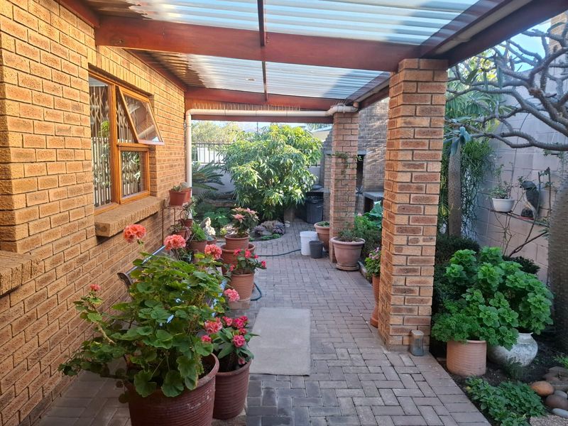 A covered brick-paved patio featuring timber beams, a corrugated roof, and a built-in brick braai, providing a functional outdoor entertainment space.