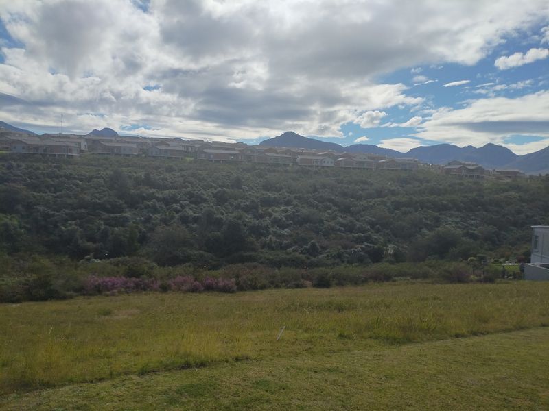 A scenic view of the surrounding landscape featuring rolling hills, natural vegetation, and distant mountain ranges under a cloudy sky.