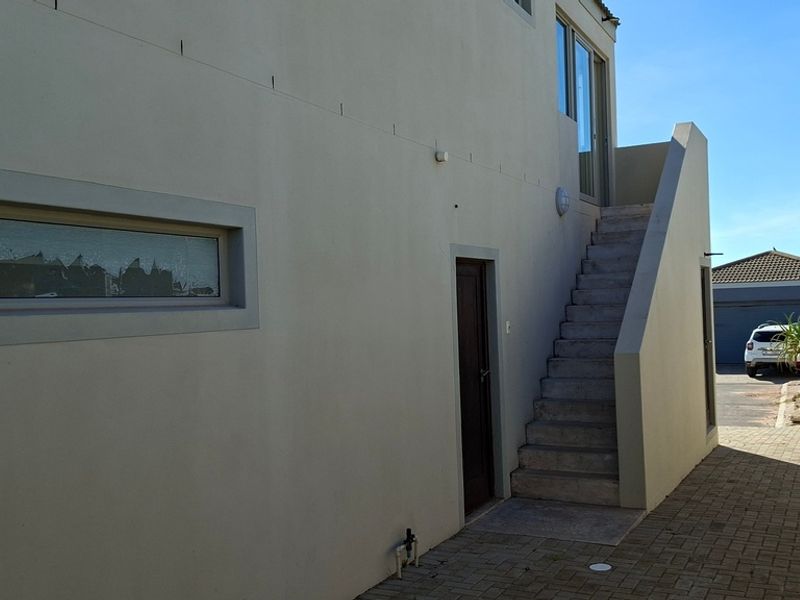 Rear exterior view of the property featuring a paved driveway, external staircase leading to an upper level, and a boundary wall.
