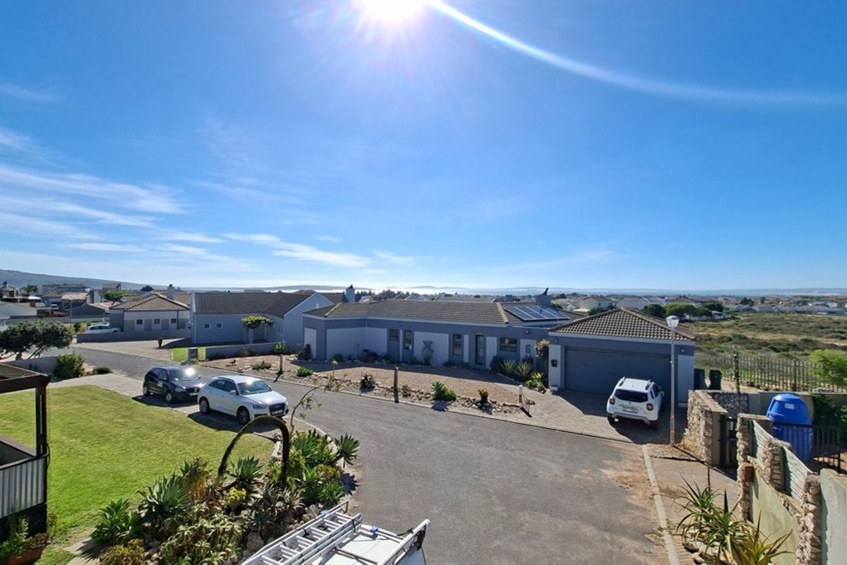 An elevated aerial view of the property showing the roof structure, solar panels, paved driveway, garage, and surrounding neighbourhood landscape.