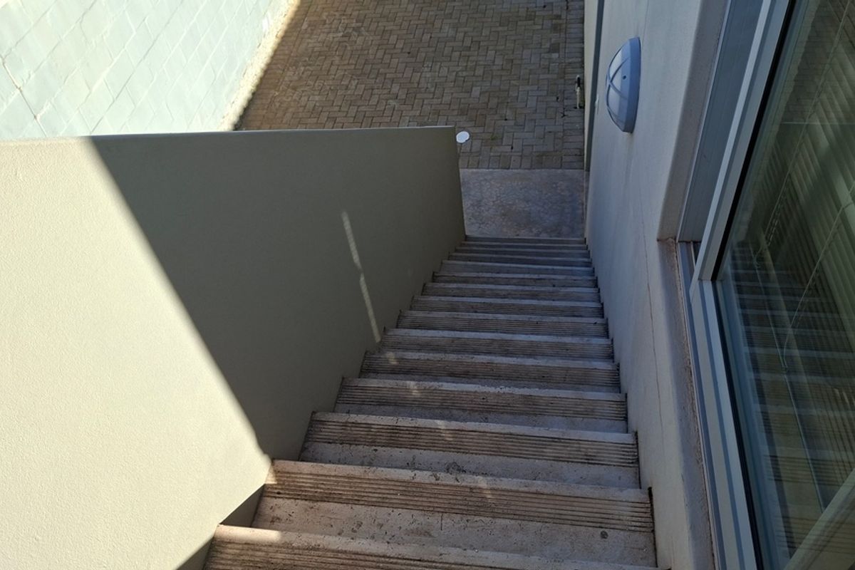 An exterior view of a concrete staircase leading down to a paved courtyard area, adjacent to a sliding glass door.
