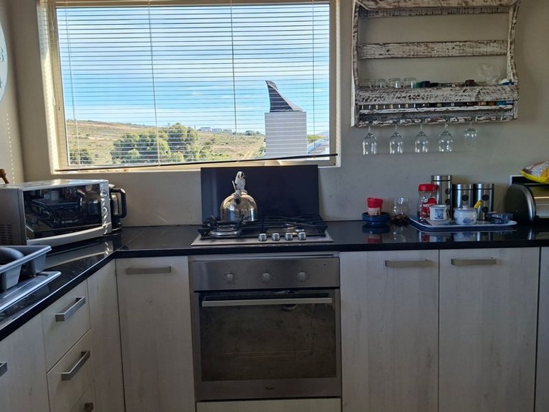 A functional kitchen featuring granite countertops, built-in oven, gas hob, and light-toned cabinetry, with a window providing natural light and views.