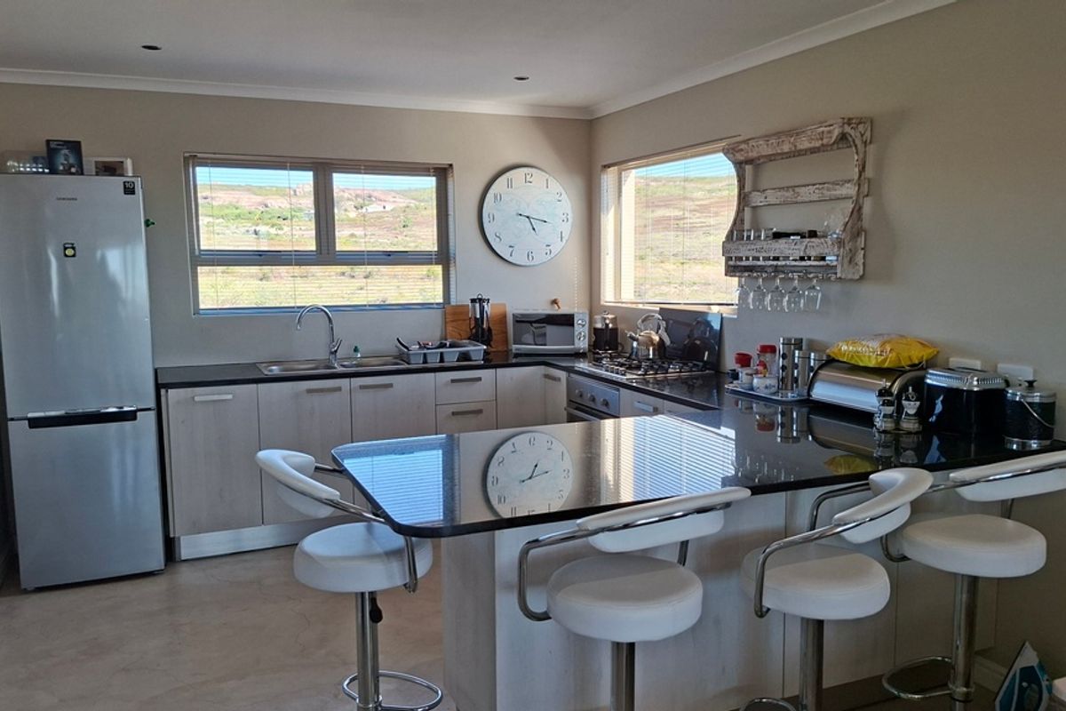 A functional kitchen featuring light-toned cabinetry, dark granite countertops, a breakfast bar, and integrated appliances with views of the surrounding landscape.