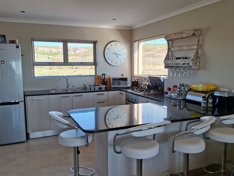 A functional kitchen featuring light-toned cabinetry, dark granite countertops, a breakfast bar, and integrated appliances with views of the surrounding landscape.