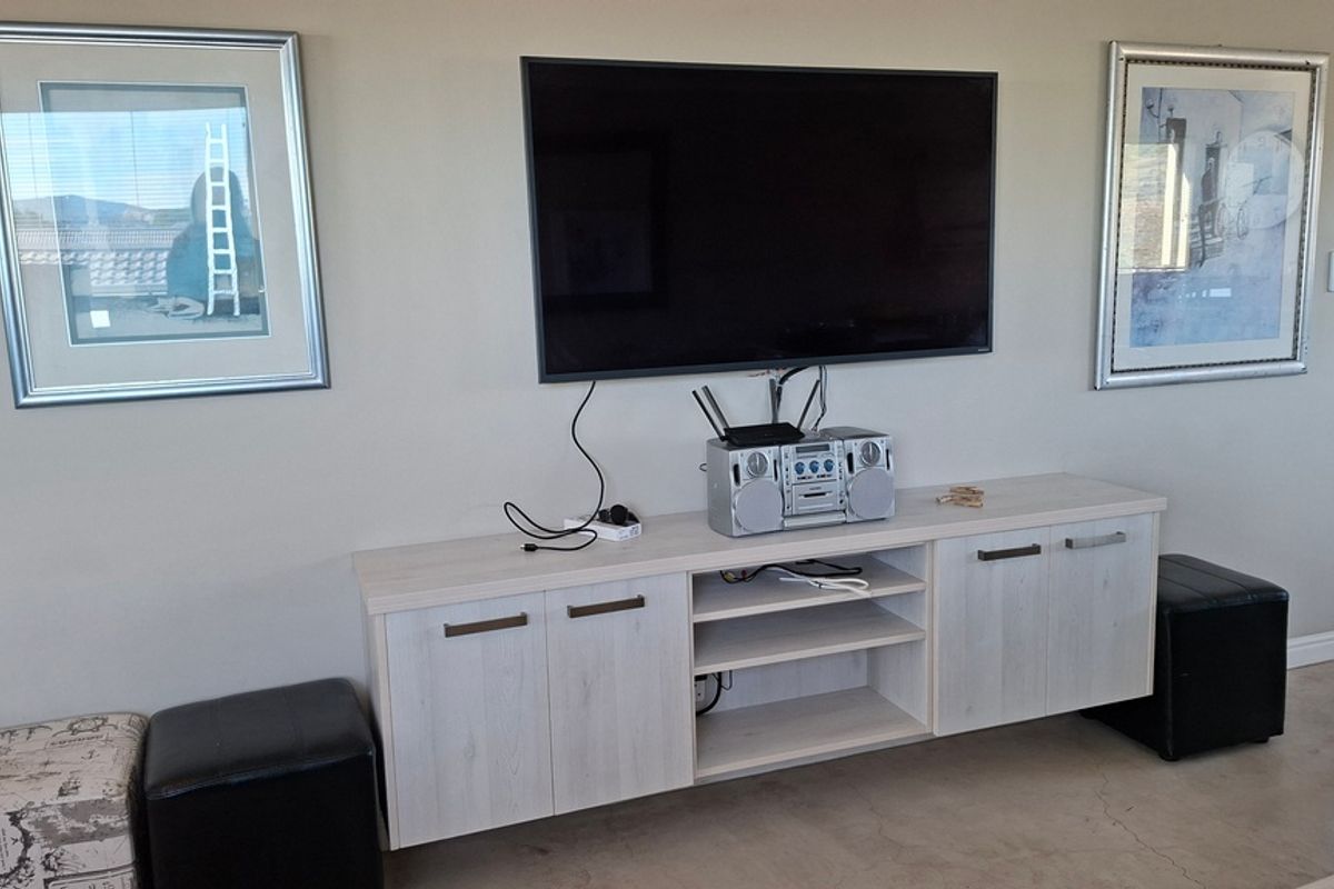 A living room area featuring a wall-mounted television, modern light-wood cabinetry, and polished concrete flooring.
