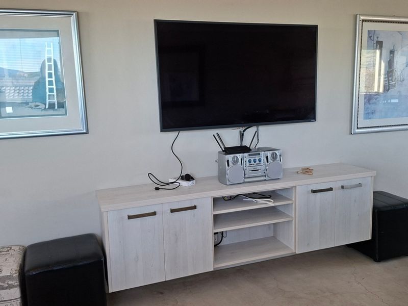 A living room area featuring a wall-mounted television, modern light-wood cabinetry, and polished concrete flooring.