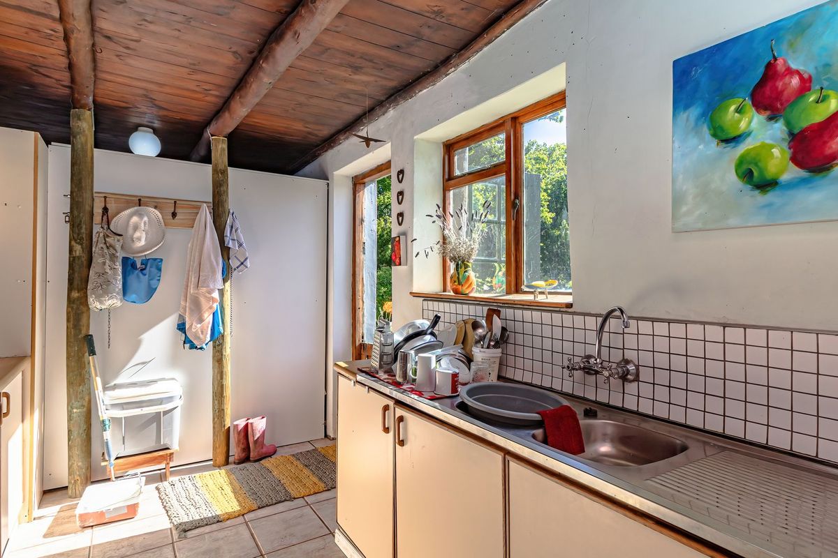 A rustic kitchen featuring exposed timber beam ceilings, tiled backsplash, and built-in cabinetry with a stainless steel sink overlooking the garden.