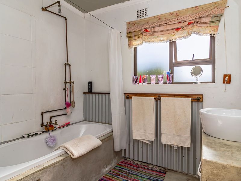 A rustic-style bathroom featuring a built-in bathtub with exposed copper plumbing, a concrete vanity with a vessel sink, and corrugated metal wall accents.
