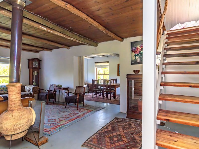 Open plan living and dining area featuring exposed timber beam ceilings, a central freestanding fireplace, and a wooden staircase leading to an upper level.