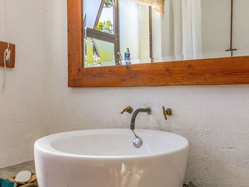 A bathroom vanity area featuring a white basin with wall-mounted brass taps and a large wooden-framed mirror against a textured plaster wall.