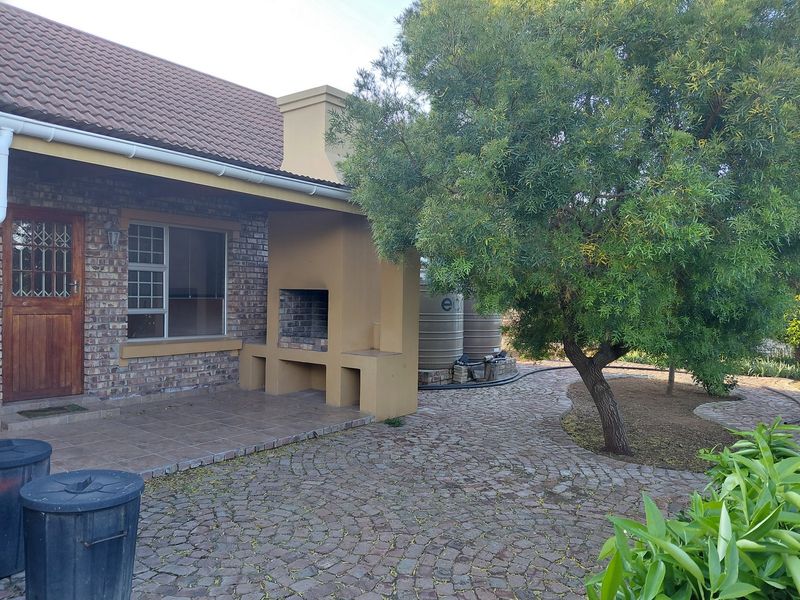 Covered patio area featuring a built-in braai, brick exterior finish, and direct access to a landscaped garden with cobblestone paving and water storage tanks.