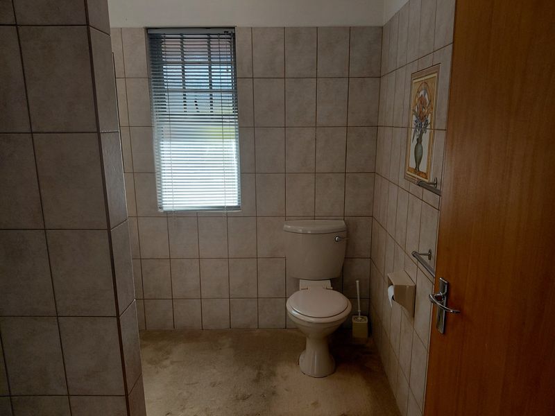 A functional bathroom featuring full-height ceramic wall tiling, a standard toilet, and a window with a fitted venetian blind.