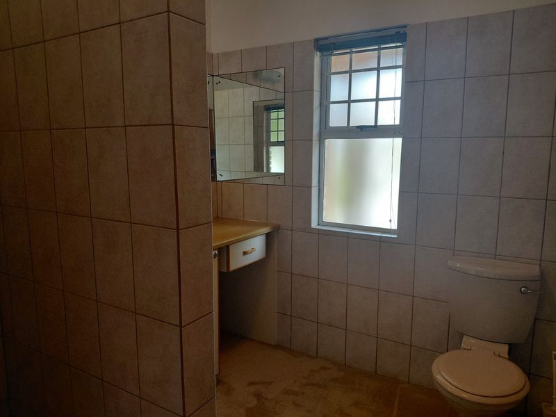A functional bathroom featuring tiled walls, a built-in vanity with a mirror, and a standard toilet, offering potential for modernization.