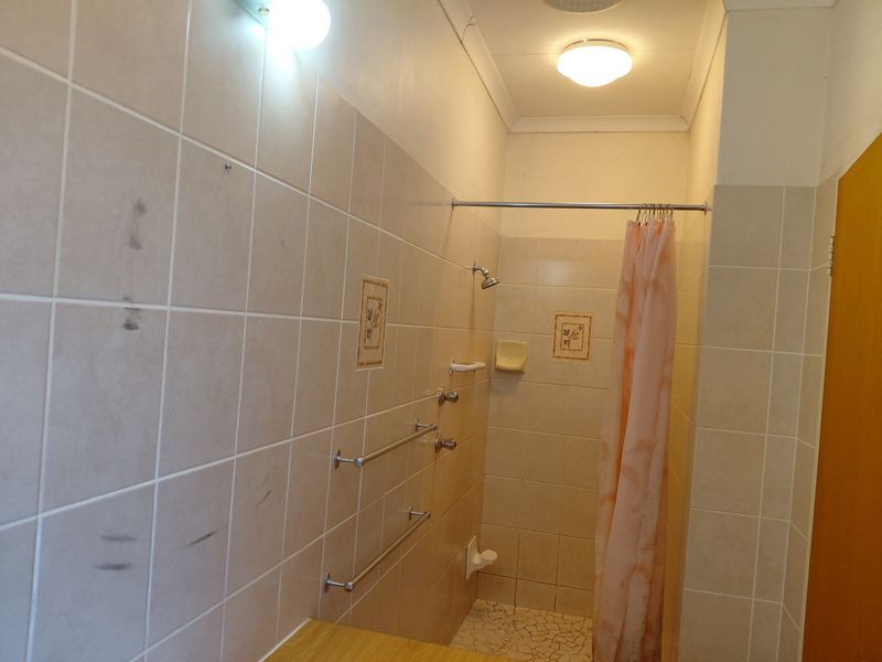 A functional bathroom shower area featuring tiled walls, a shower mixer, and built-in towel rails.