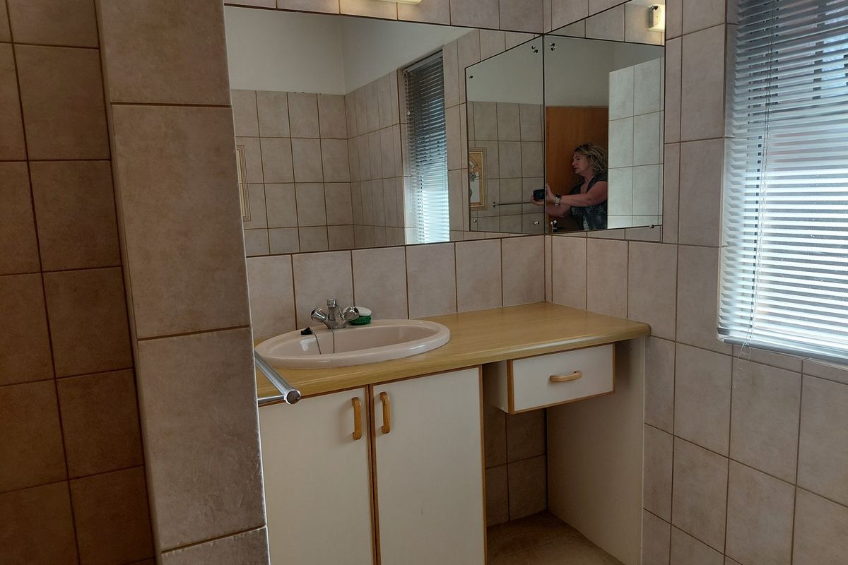A functional bathroom vanity area featuring a drop-in sink, built-in cabinetry, wall-mounted mirror, and neutral tiled wall finishes.