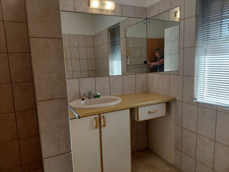 A functional bathroom vanity area featuring a drop-in sink, built-in cabinetry, wall-mounted mirror, and neutral tiled wall finishes.