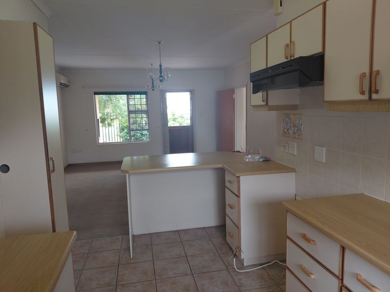 Open-plan kitchen and living area featuring tiled kitchen flooring, built-in cabinetry, and carpeted living space with access to an exterior door.