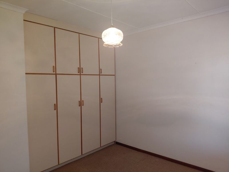 A clean, empty bedroom featuring neutral walls, carpeted flooring, and extensive built-in cupboard storage with a classic pendant light fixture.