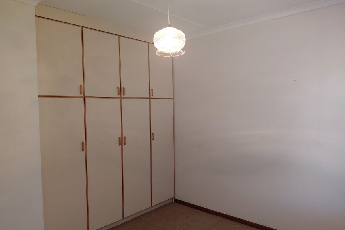 A clean, empty bedroom featuring neutral walls, carpeted flooring, and extensive built-in cupboard storage with a classic pendant light fixture.