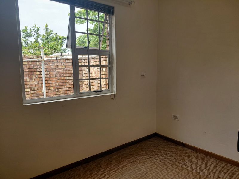 An empty bedroom featuring carpet flooring and an aluminium window frame, showing visible wall cracks requiring maintenance.