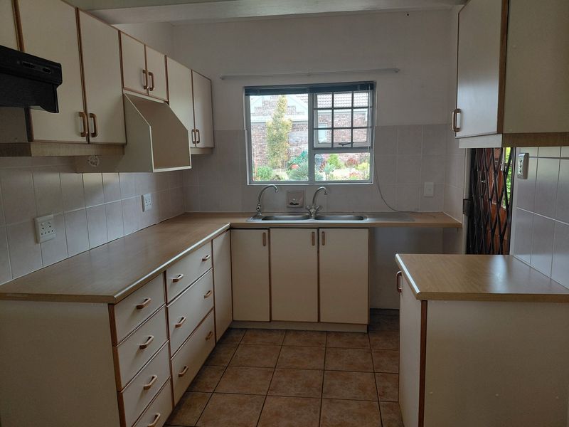 A functional kitchen featuring laminate countertops, double basin sink, tiled backsplash, and ample built-in cabinetry with a neutral aesthetic.