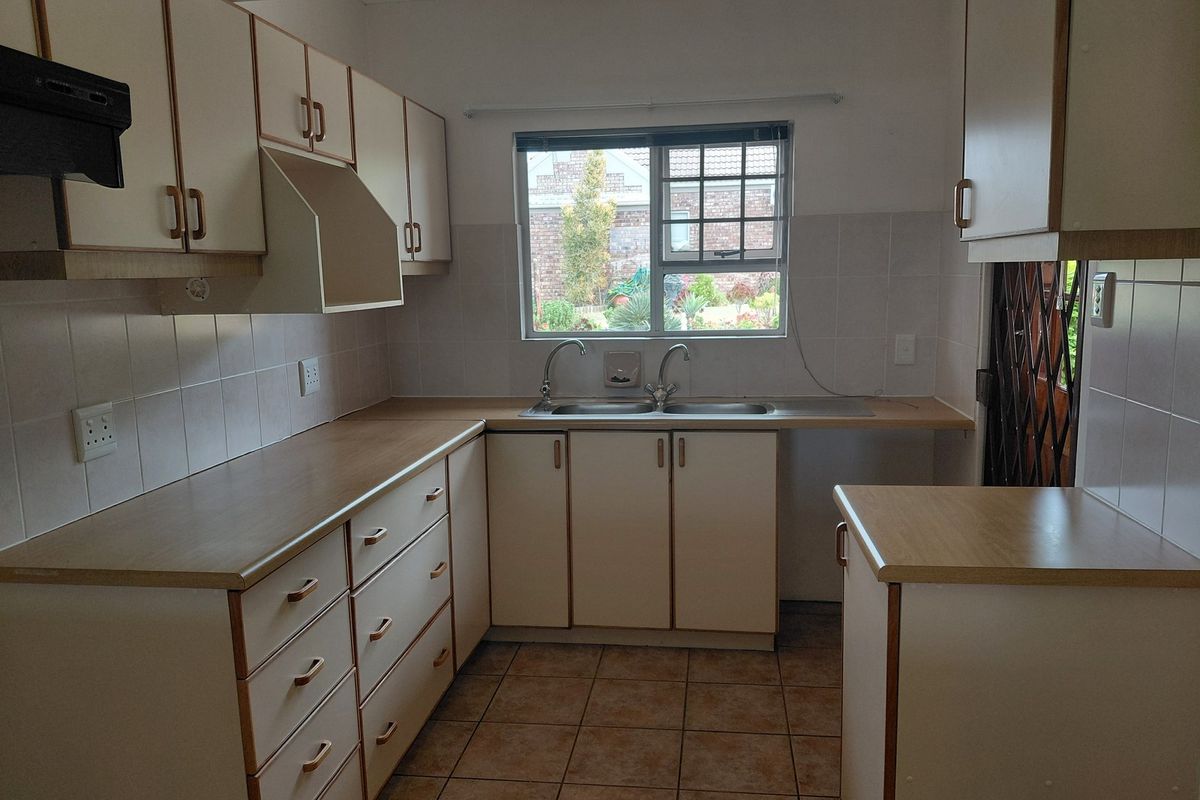 A functional kitchen featuring laminate countertops, double basin sink, tiled backsplash, and ample built-in cabinetry with a neutral aesthetic.