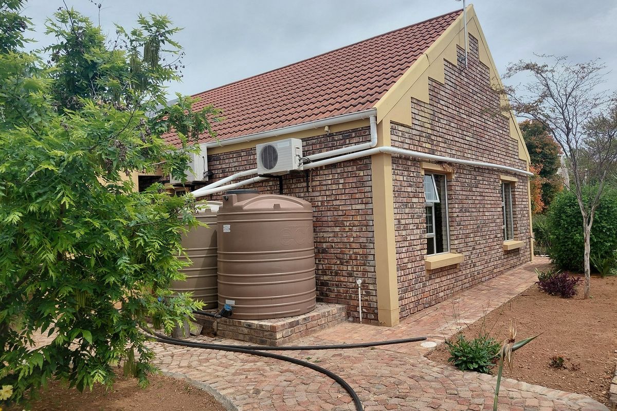 Rear view of a face brick house featuring a tiled roof, paved garden pathways, and installed water storage tanks with an external air conditioning unit.