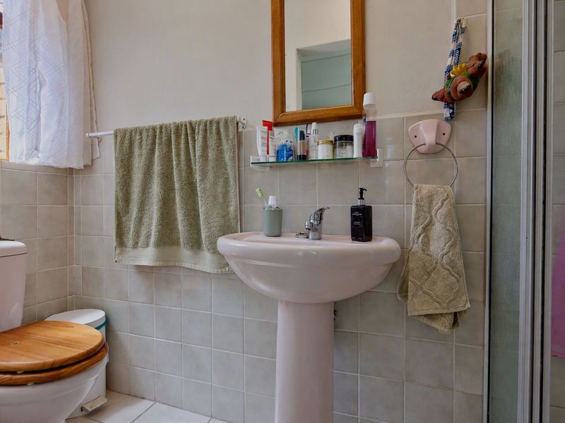 A functional bathroom featuring a pedestal basin, toilet, and shower enclosure with neutral wall tiling.