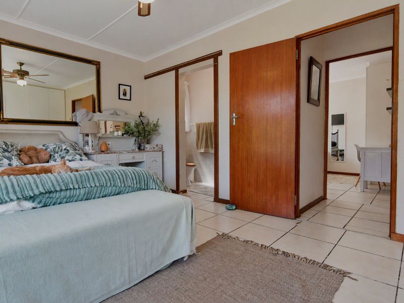 A bedroom featuring tiled flooring, a ceiling fan, and direct access to an en-suite bathroom with wooden door frames.