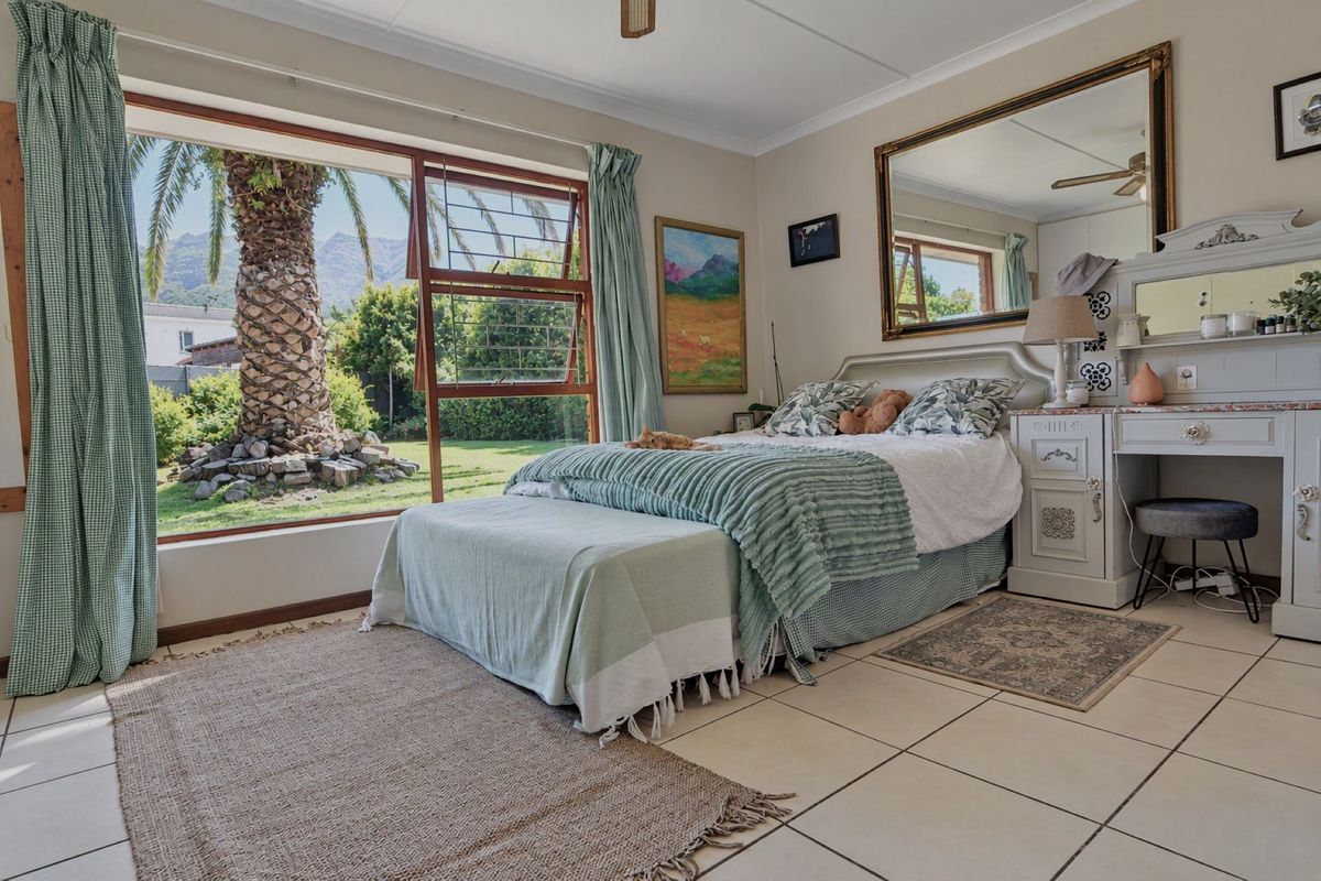 A bright bedroom featuring large windows with garden views, tiled flooring, a ceiling fan, and a built-in vanity unit.