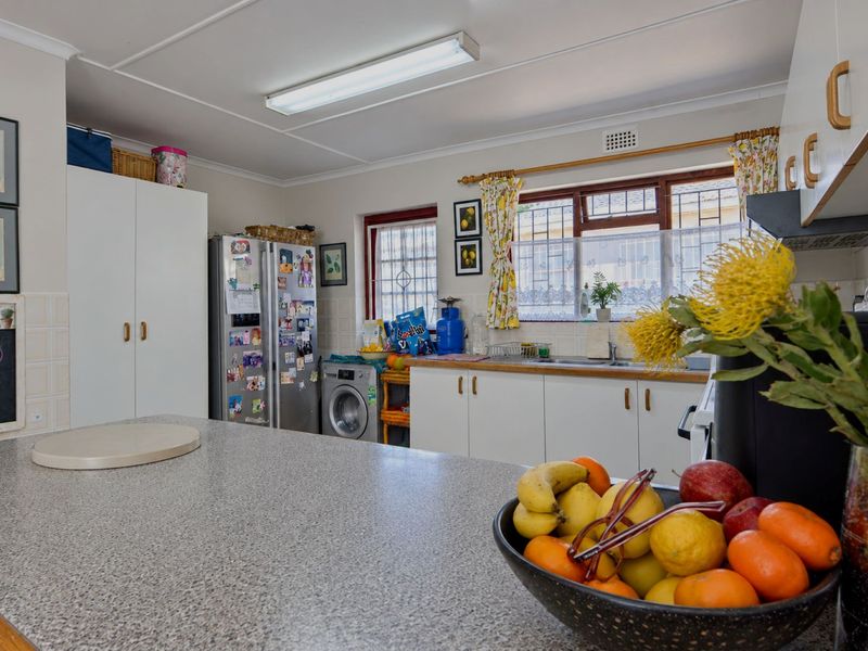 A functional kitchen featuring white cabinetry, laminate countertops, a double sink, and a tiled backsplash, with integrated space for laundry appliances.