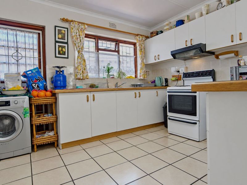 A functional kitchen featuring white cabinetry, laminate countertops, tiled flooring, and a built-in extractor fan, with space for laundry appliances.