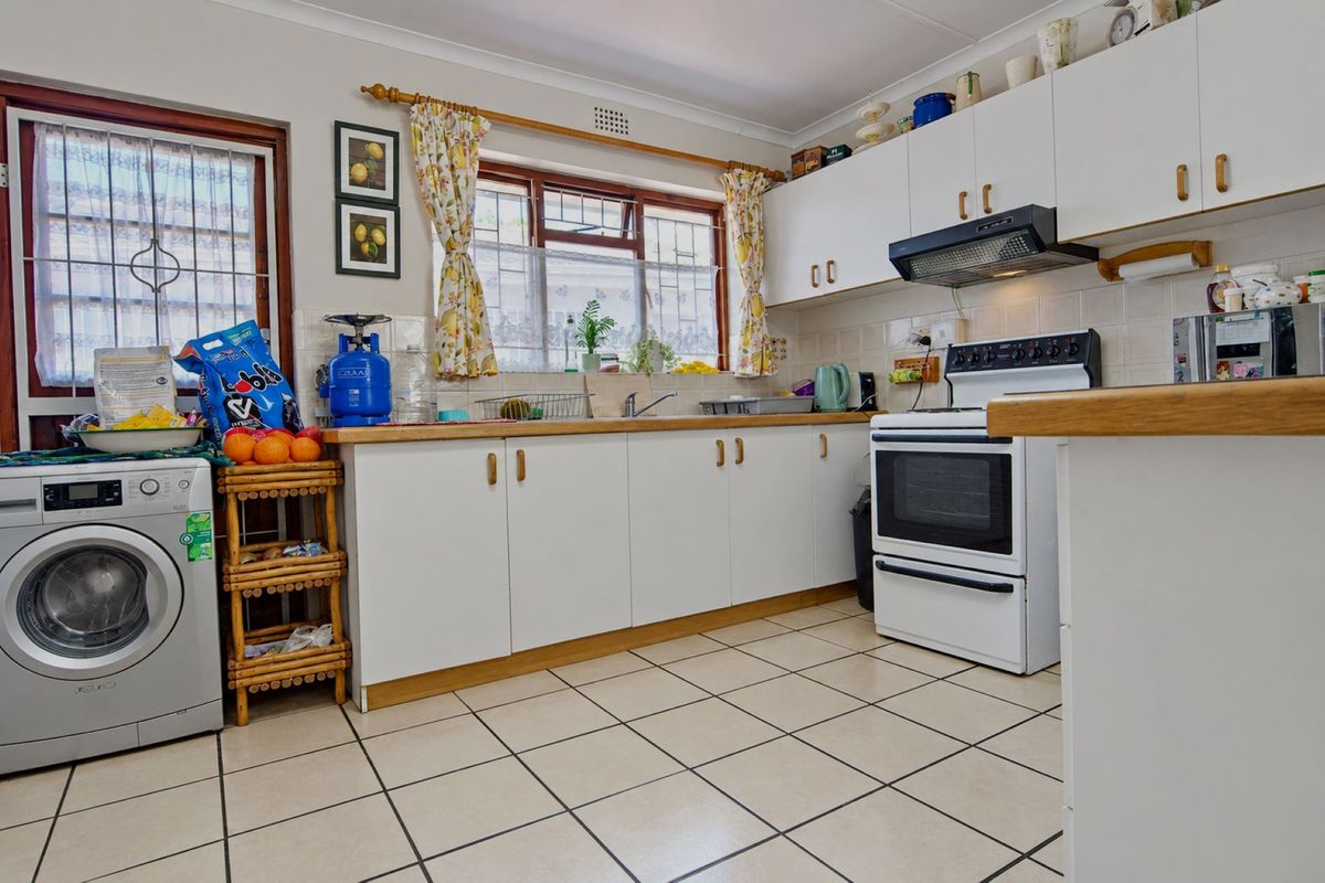 A functional kitchen featuring white cabinetry, laminate countertops, tiled flooring, and a built-in extractor fan, with space for laundry appliances.