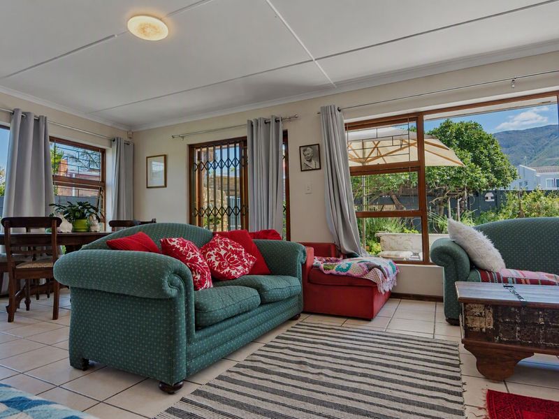 A bright living room featuring tiled flooring, large windows, and a sliding glass door providing access to the garden area.