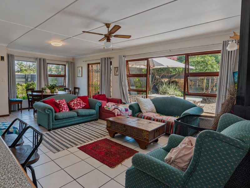 Spacious open-plan living and dining area featuring tiled flooring, a ceiling fan, and large windows providing natural light and garden views.