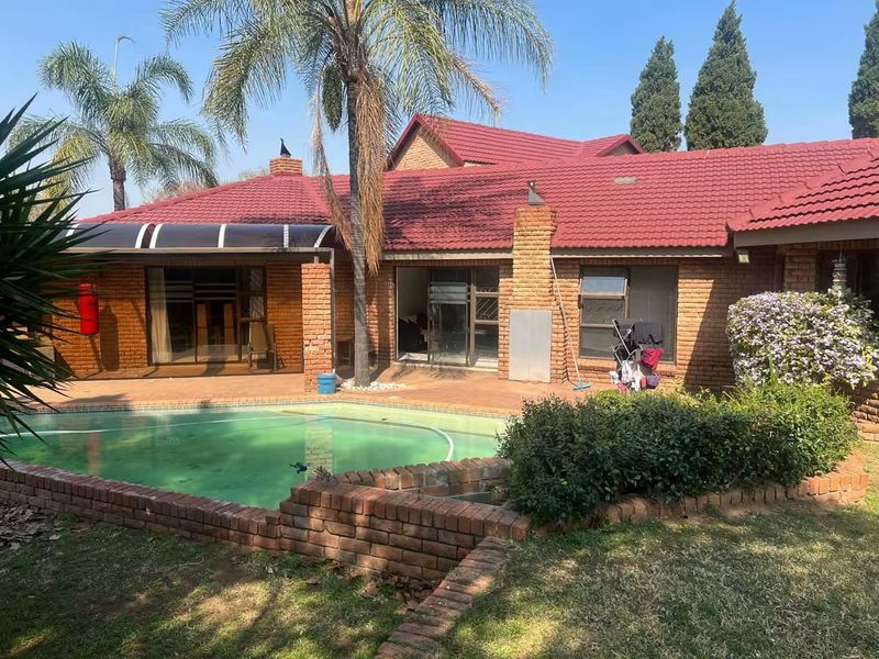 Rear exterior view featuring a swimming pool, brick patio, covered outdoor area, and traditional brick house facade with a tiled roof.