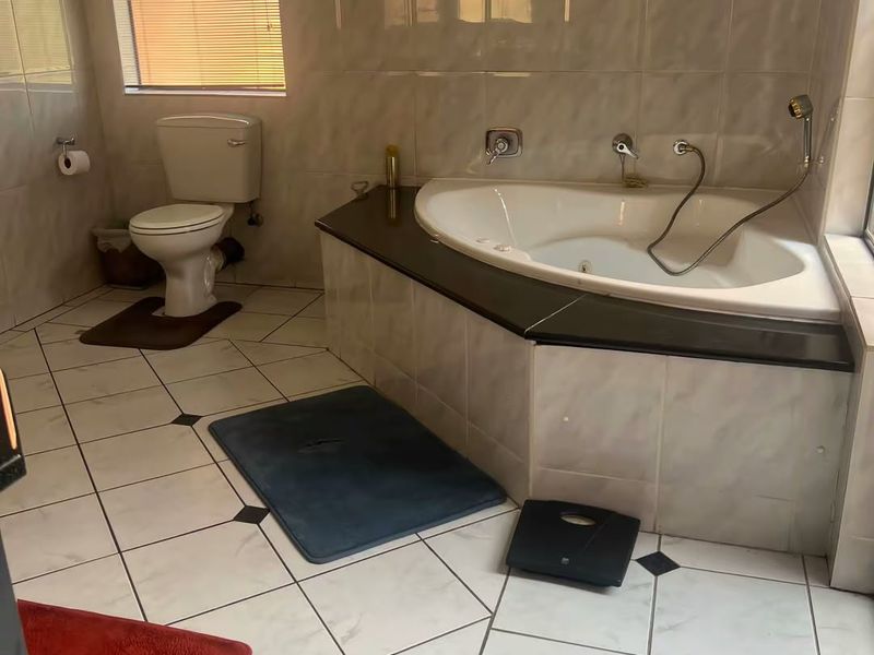 A functional bathroom featuring a corner bathtub, toilet, and full-height wall tiling with diamond-patterned floor tiles.