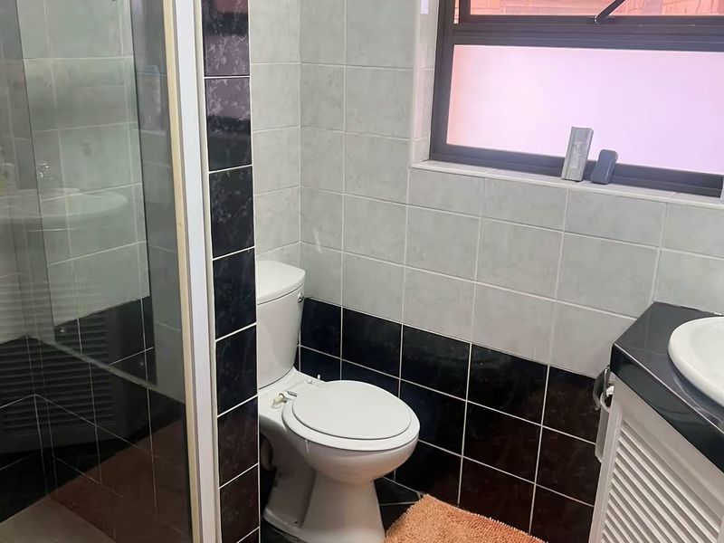 A functional bathroom featuring a glass shower enclosure, a vanity with a basin, and contrasting black and white wall tiling.