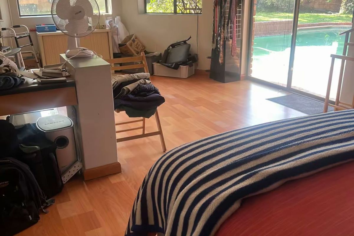 Spacious bedroom featuring laminate flooring, a split-system air conditioner, and large sliding glass doors providing direct access to the pool area.