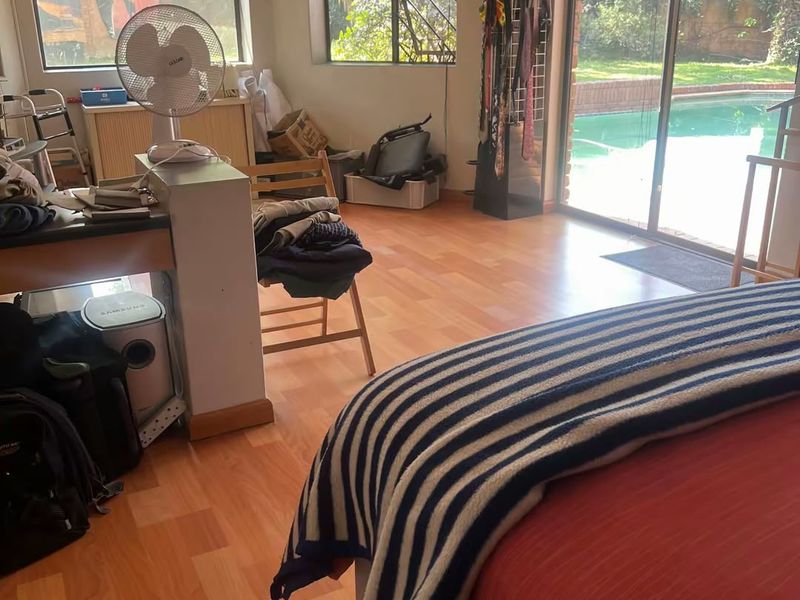 Spacious bedroom featuring laminate flooring, a split-system air conditioner, and large sliding glass doors providing direct access to the pool area.
