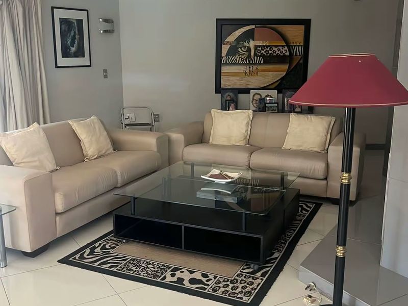 A well-maintained living room featuring neutral tiled flooring, recessed lighting, and a fireplace hearth, offering a comfortable and functional space.