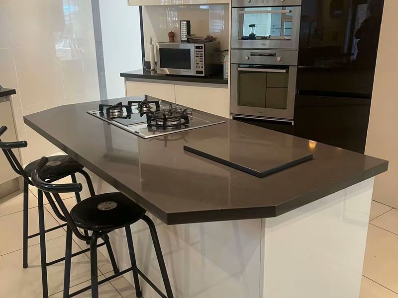 Modern kitchen featuring a central island with a gas cooktop, high-gloss cabinetry, built-in oven, microwave, and sleek stone countertops with tiled flooring.