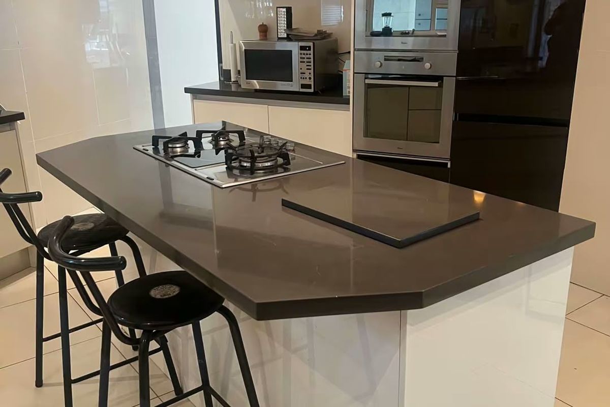 Modern kitchen featuring a central island with a gas cooktop, high-gloss cabinetry, built-in oven, microwave, and sleek stone countertops with tiled flooring.