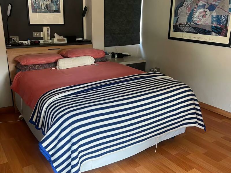 A bedroom featuring laminate flooring, a built-in headboard unit, and a roller blind.