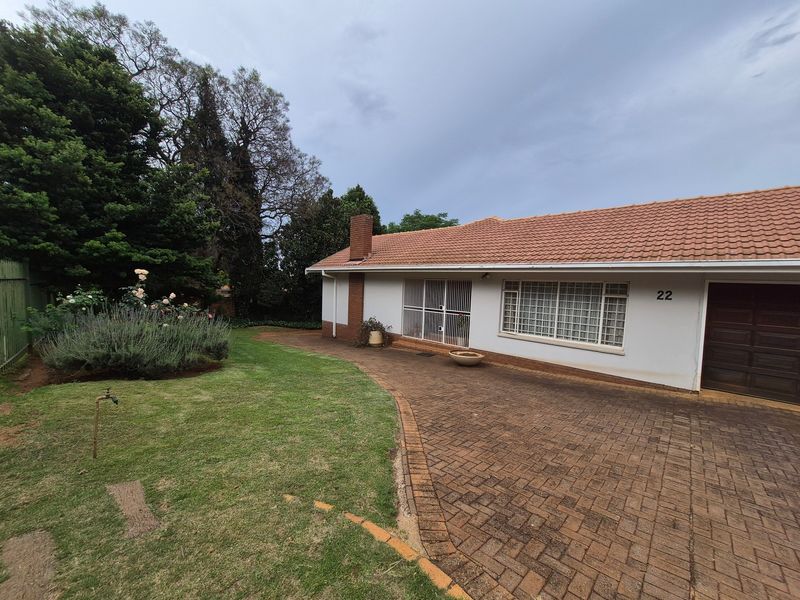 Front view of a single-story house featuring a brick driveway, tiled roof, and established garden area.