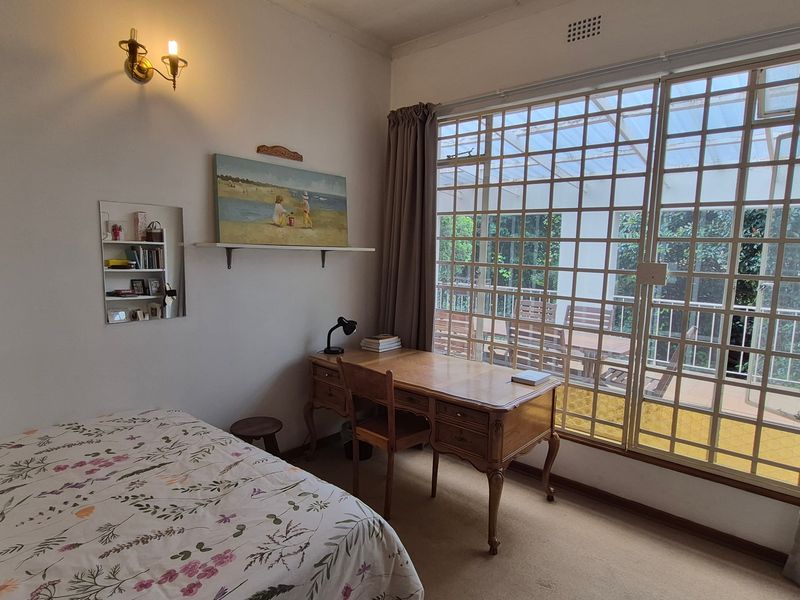 A bedroom featuring carpeted flooring, a wall-mounted light fixture, and a large sliding glass door with a security grille providing access to the patio.