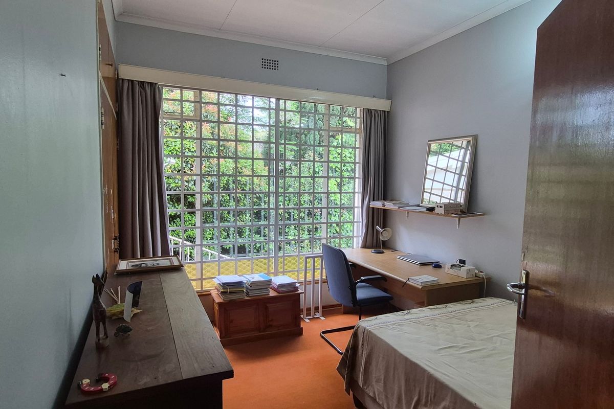 A functional bedroom featuring built-in cupboards, carpeted flooring, and a large window with a grid design, offering natural light and garden views.