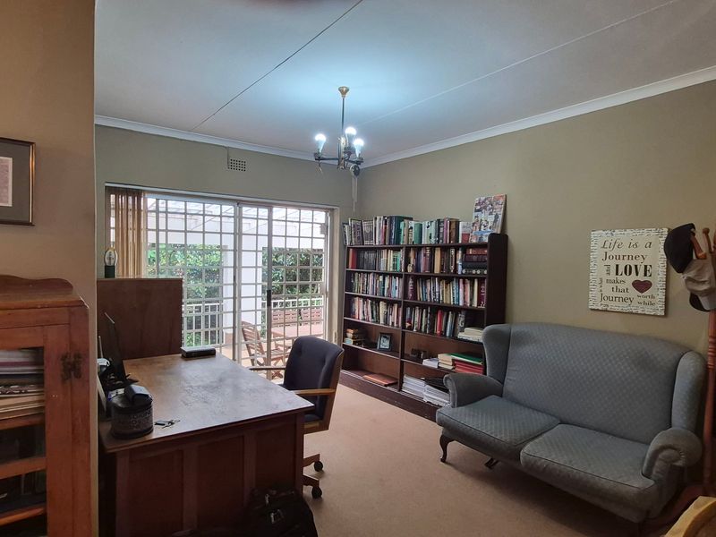 A functional home office space featuring carpeted flooring, a ceiling light fixture, and a sliding glass door with security gate leading to the patio.